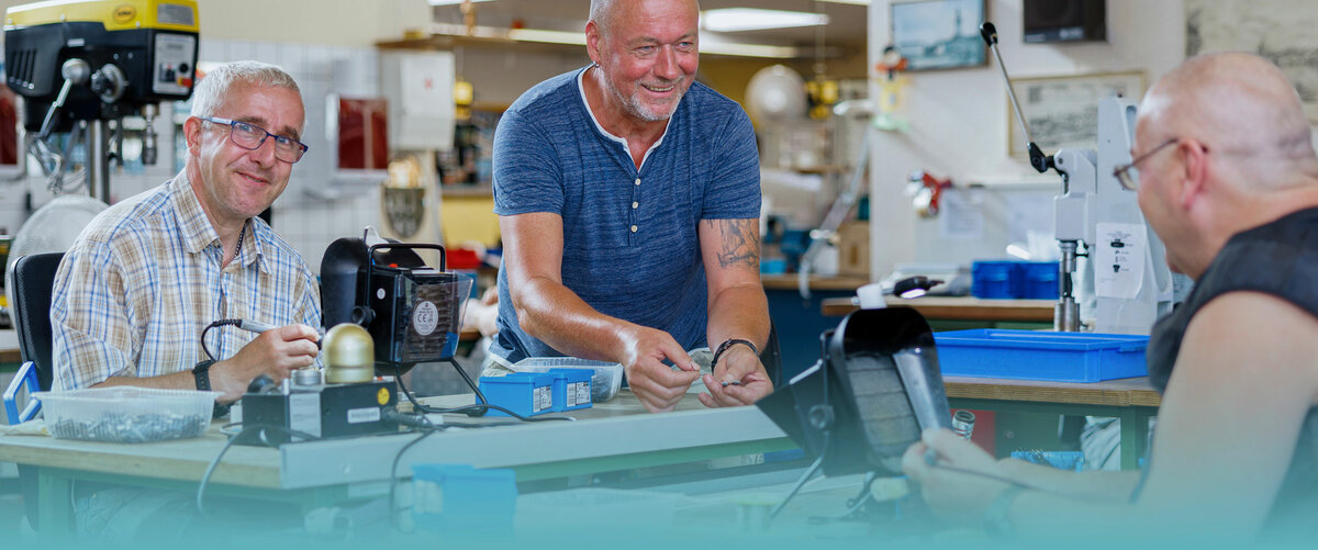 Drei Personen sitzen in einer Werkstatt und bauen Teile zusammen.